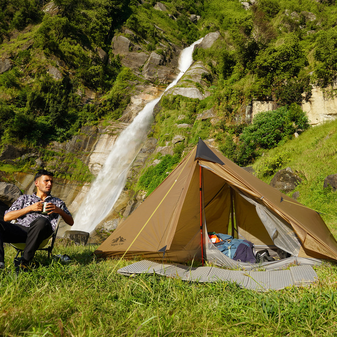 Night Cat 2 Person Tent in Khaki pitched beside a waterfall with a camper relaxing nearby, sleeping gear visible inside the open tent 