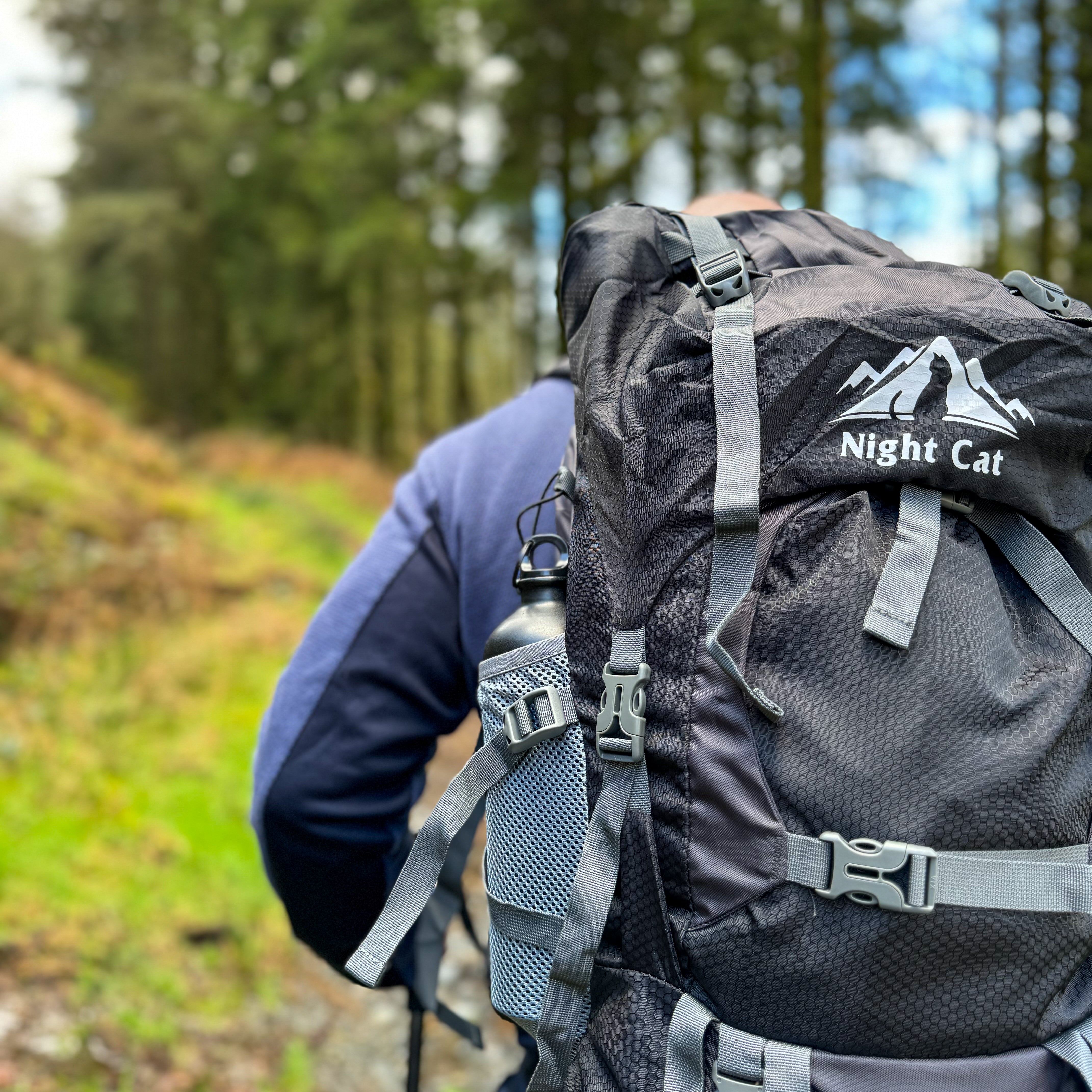 Close-up of a hiker wearing a Night Cat hiking backpack with water bottle in side pocket, walking through a forest trail, promoting durable and reliable hiking bags and backpacks.