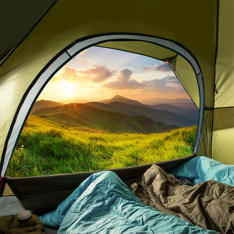 View from inside a tent overlooking a beautiful sunset in the mountains, showcasing a camping adventure setup with sleeping bags and outdoor gear.