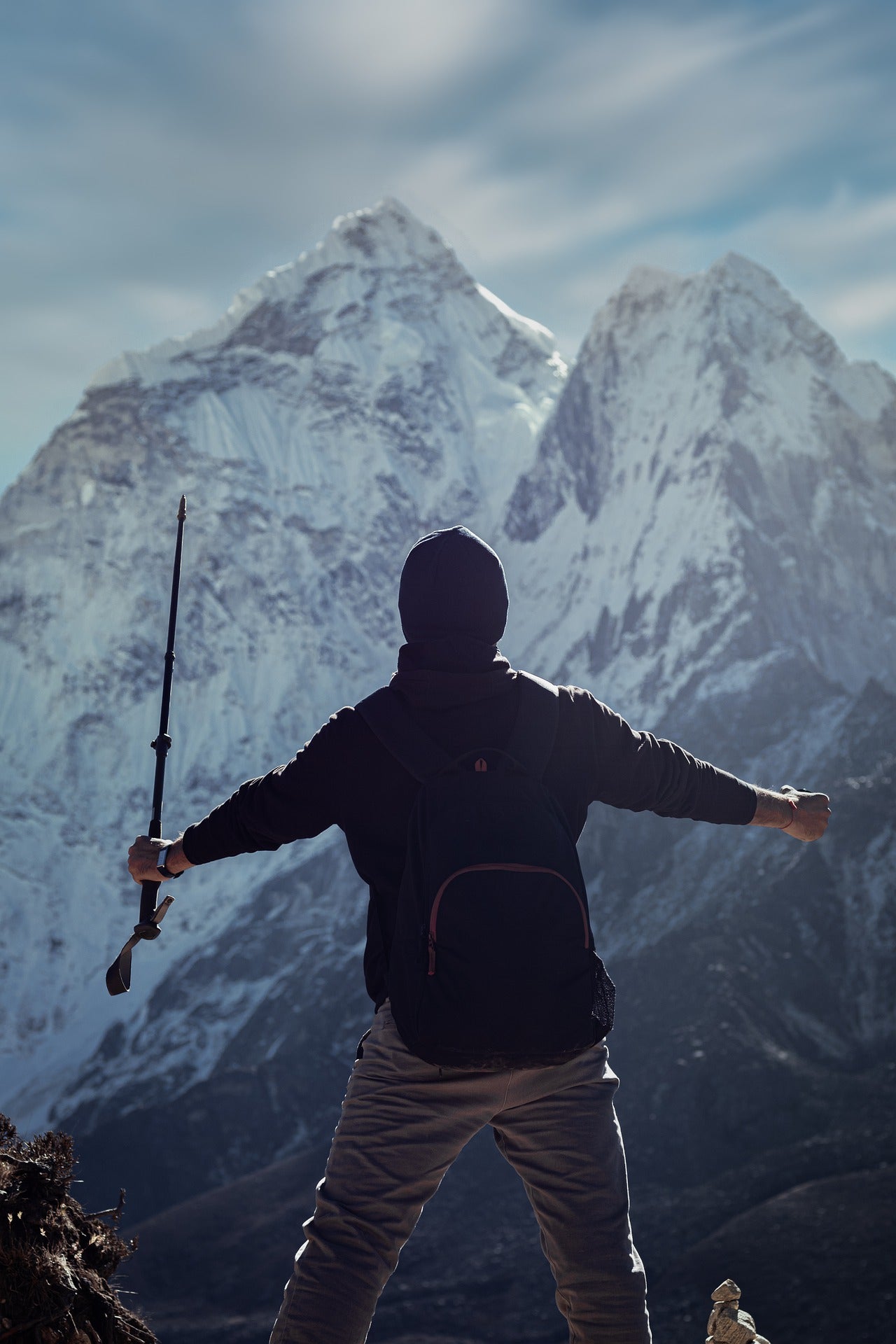 Back view of a hiker standing with a trekking pole, looking out at snow-capped mountains, showcasing outdoor adventure accessories for mountain exploration.