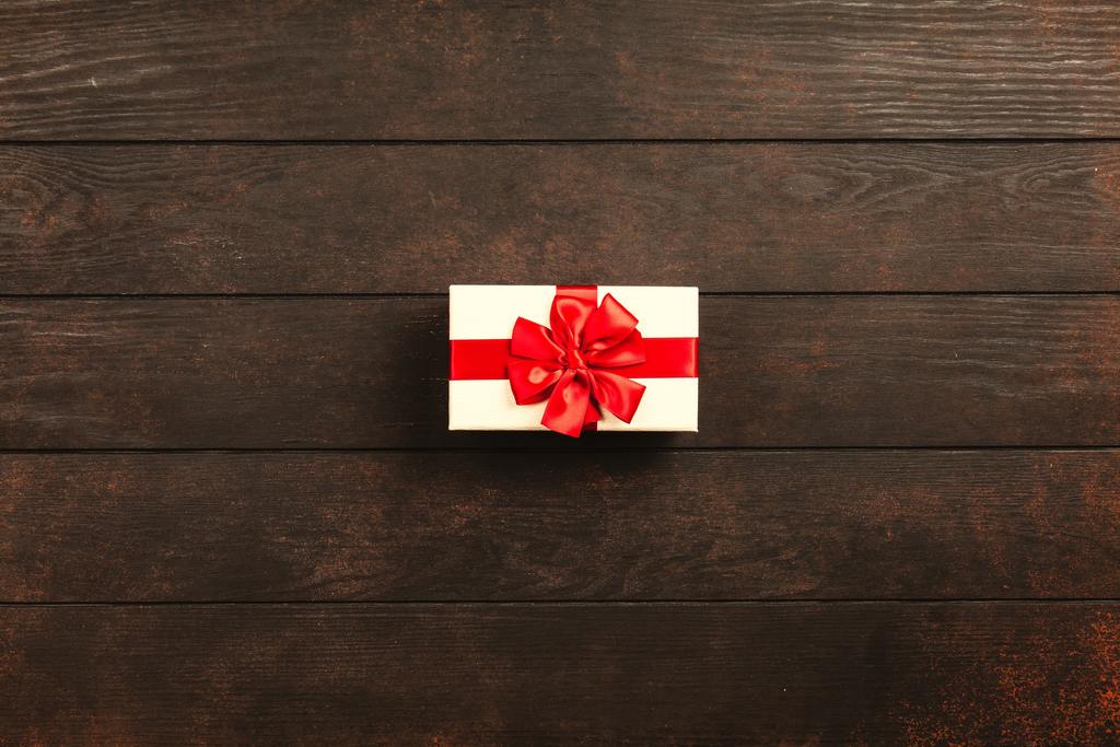 Beautifully wrapped gift box with a red ribbon placed on a dark wooden surface, symbolising gift cards or gift vouchers.