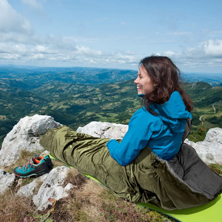 Woman sitting in the Night Cat sleeping bag on a rocky mountain top