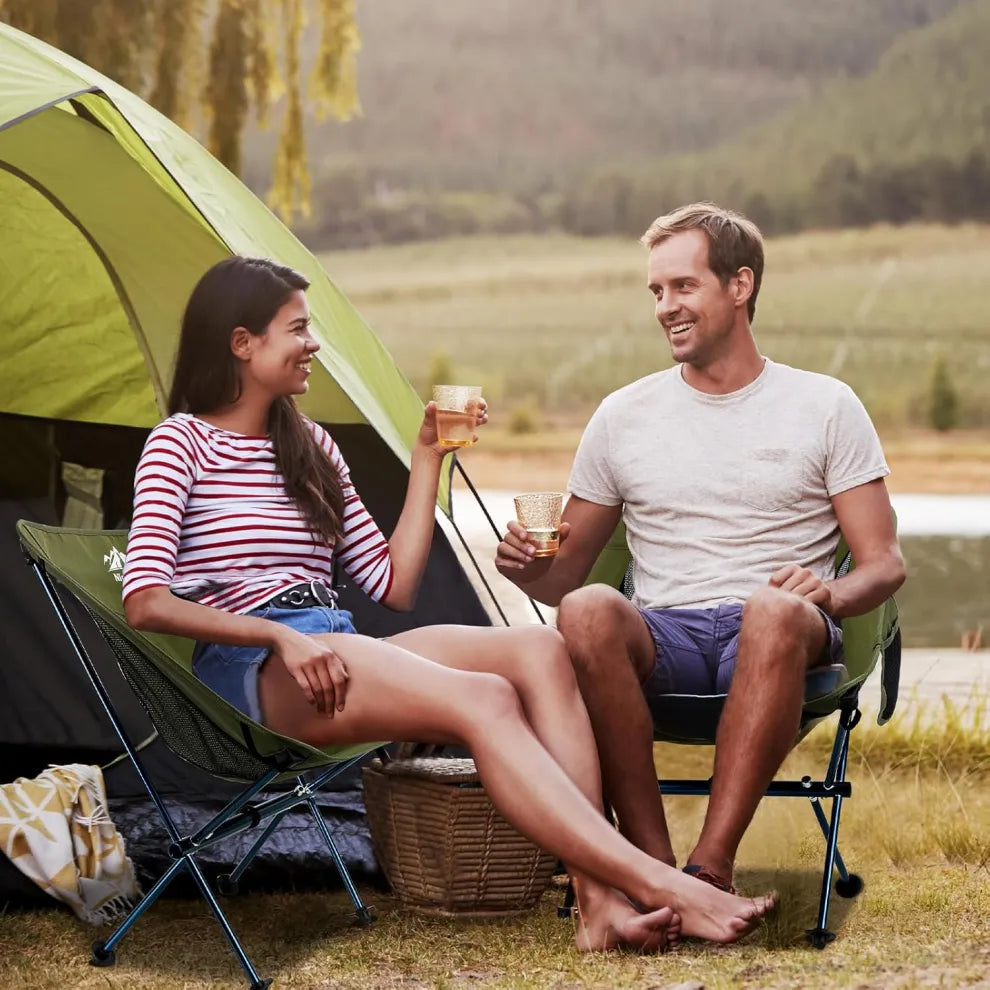 A couple relaxing in Night Cat camping chairs while enjoying drinks outdoors, with a tent in the background, illustrating a peaceful camping experience.