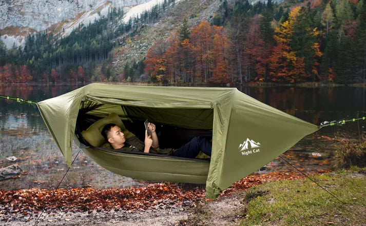 Person relaxing in the Night Cat hammock tent beside an autumn lake